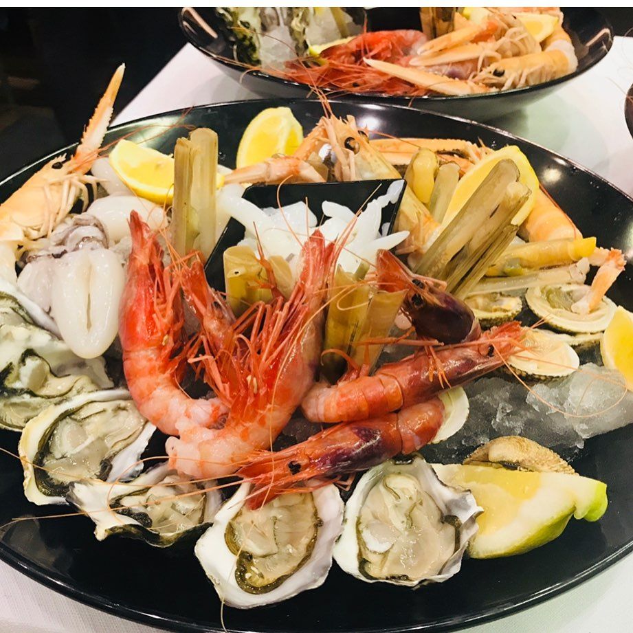 Piatto di frutti di mare: ostriche, gamberi, vongole, cannolicchi, spicchi di limone su un piatto nero con ghiaccio.