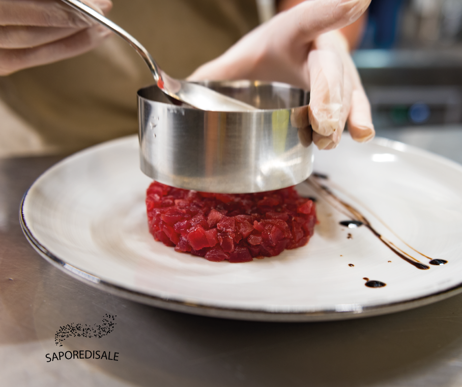 Uno chef con i guanti usa uno stampo ad anello di metallo per dare forma a un piatto rosso con salsa su un piatto bianco.