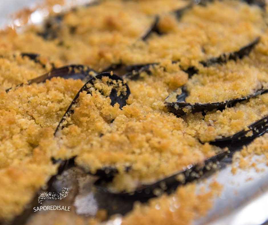 Cozze al forno ricoperte di pangrattato dorato su una teglia.