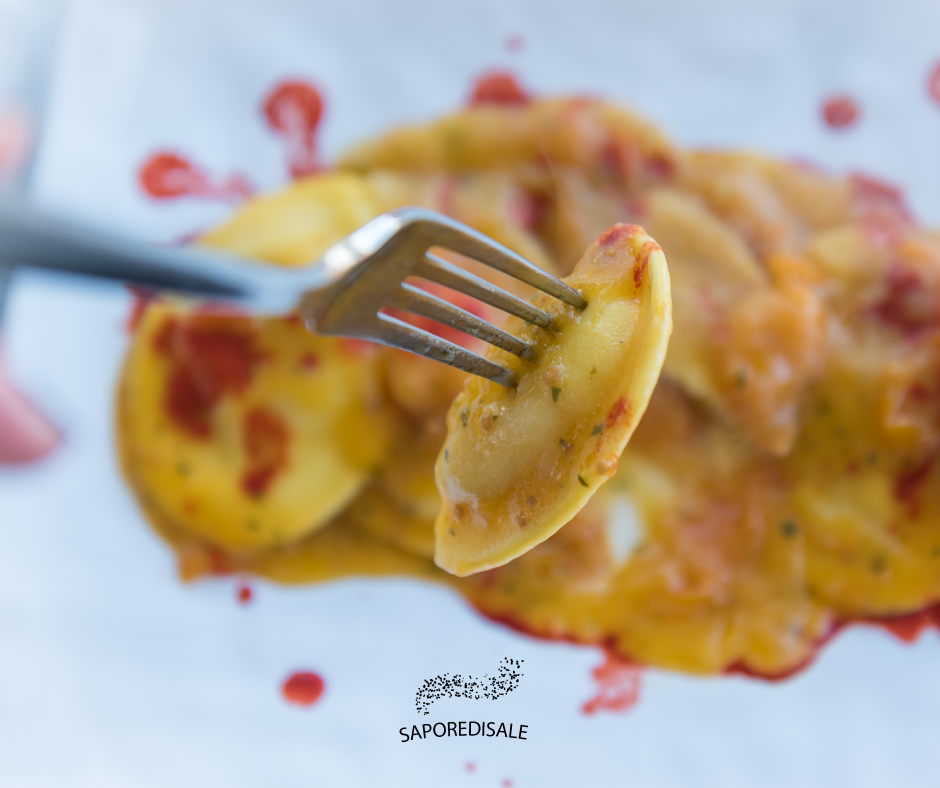 Forchetta che solleva un raviolo ricoperto di salsa da un piatto.
