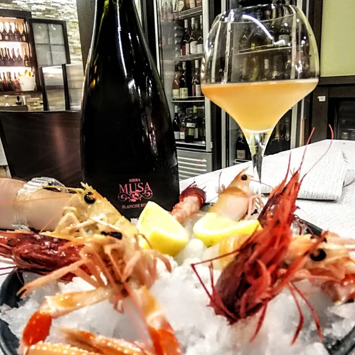 Frutti di mare su ghiaccio con bicchiere di vino e bottiglia; primo piano di gamberi, limone e una bevanda chiara in un ristorante.