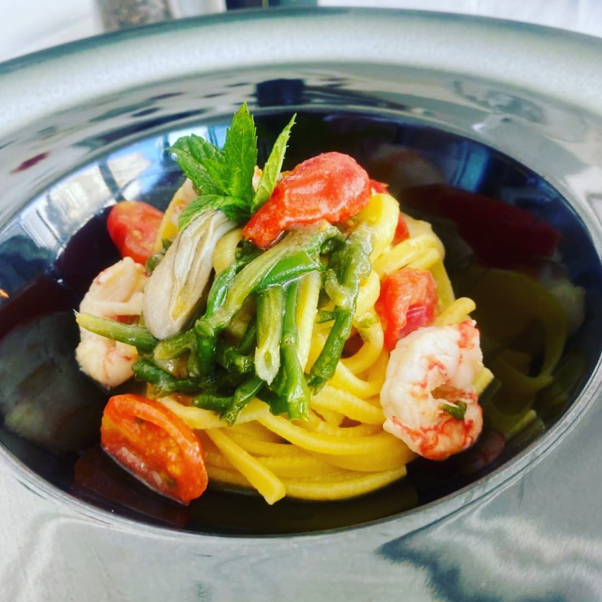 Piatto di pasta con gamberi, pomodori, fagiolini e menta in una ciotola d'argento.
