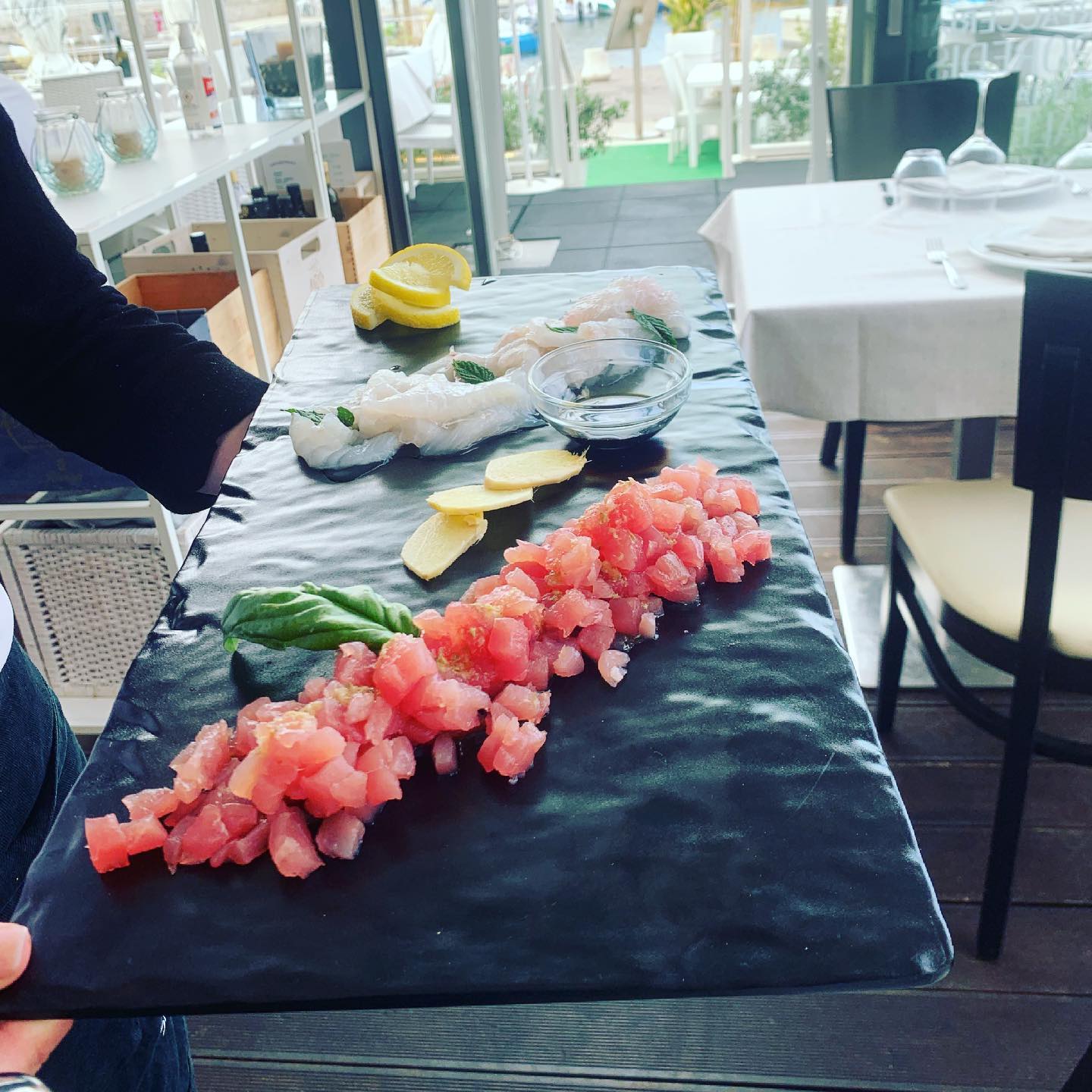 Un cameriere tiene in mano un piatto di pesce crudo e ingredienti, servito in un ristorante.