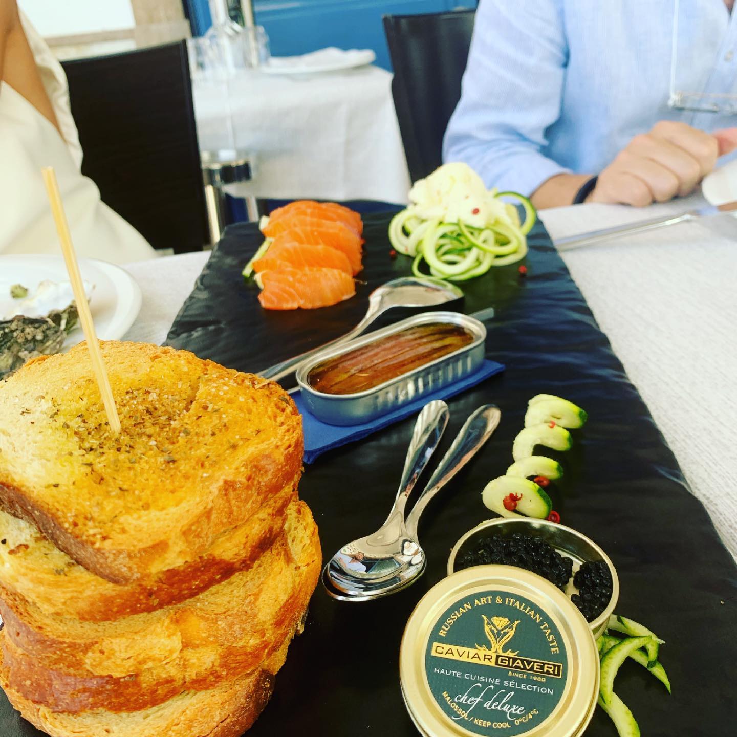 Un piatto di cibo servito in un ristorante comprende toast, salmone, caviale, acciughe e cetriolo.