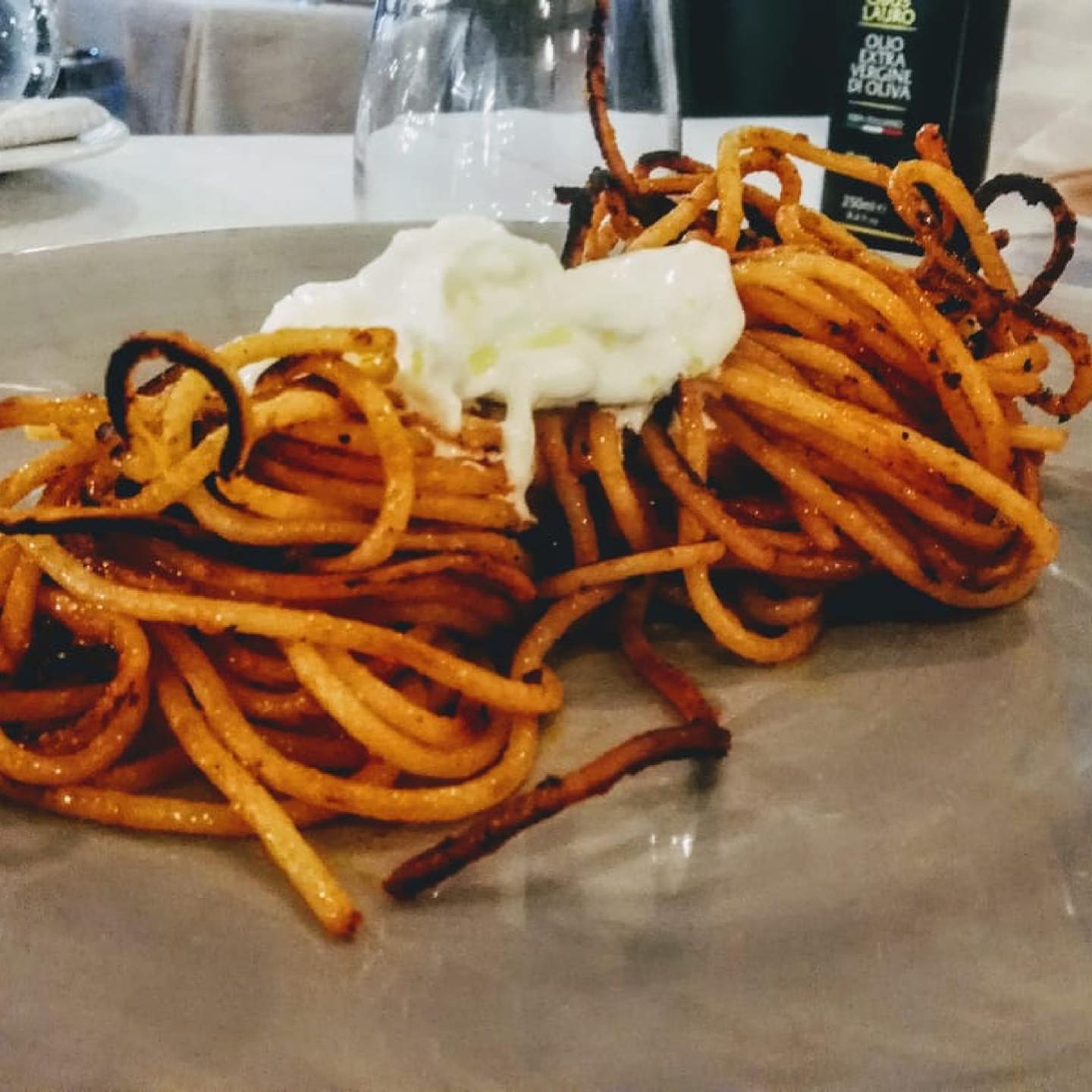 Piatto di pasta con besciamella, tagliatelle marroni e bordi scuri e croccanti su un piatto grigio.
