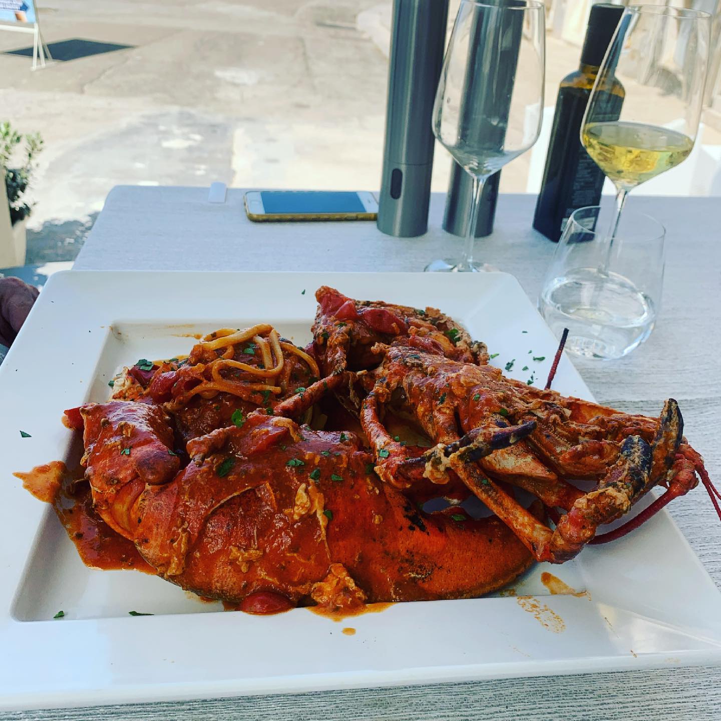 Piatto di pasta e aragosta su un piatto bianco, con bicchieri di vino e condimenti su un tavolo.