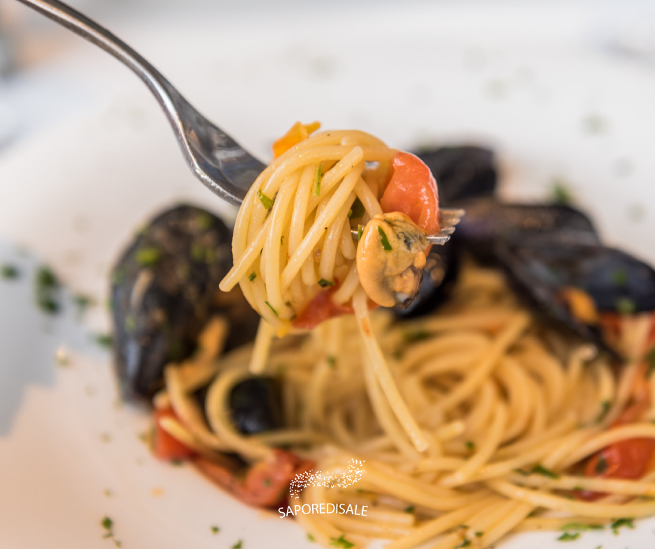 Piatto di spaghetti con cozze e pomodori, con la forchetta che solleva un ricciolo di pasta.