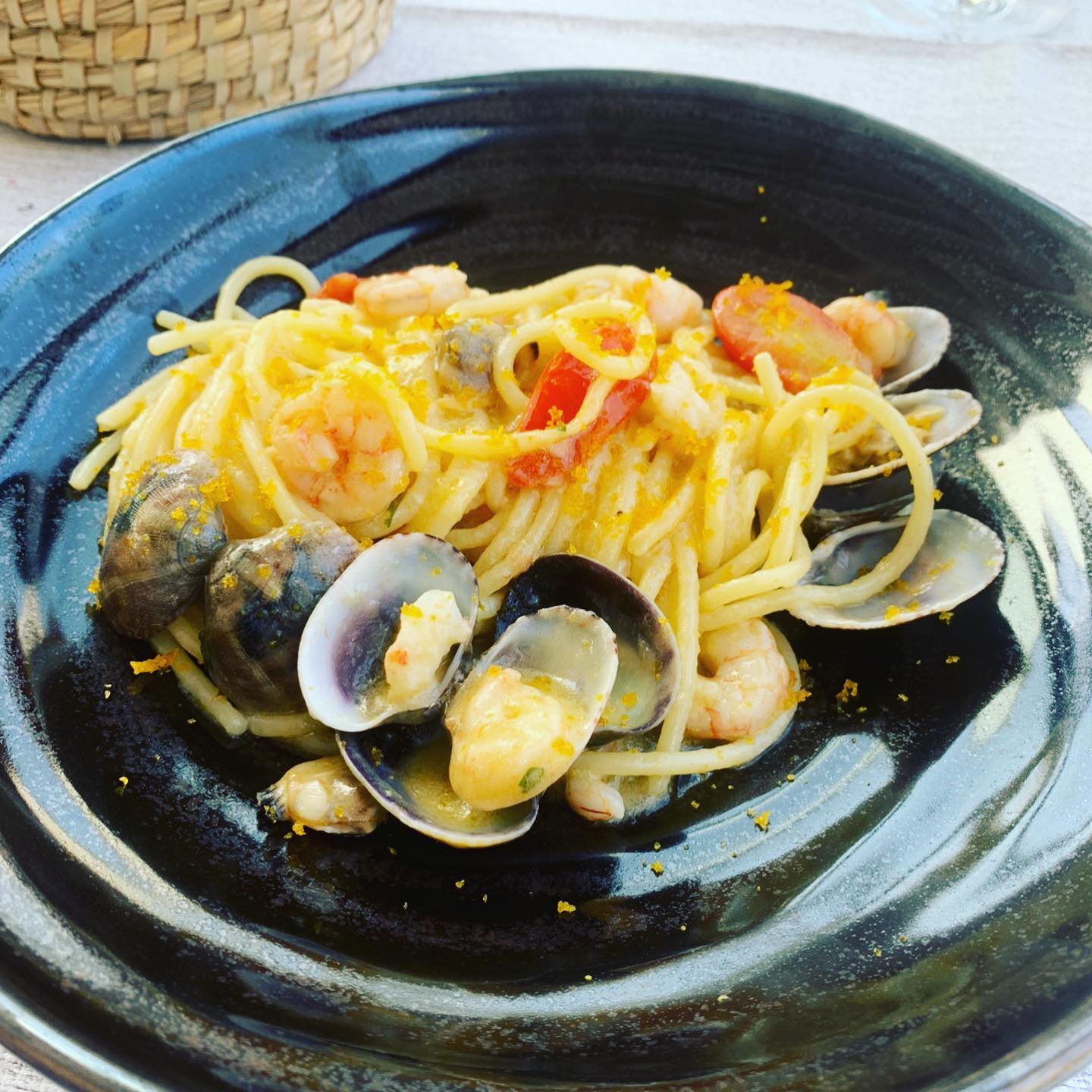 Spaghetti ai frutti di mare: vongole, gamberi e pomodori, in una ciotola nera.