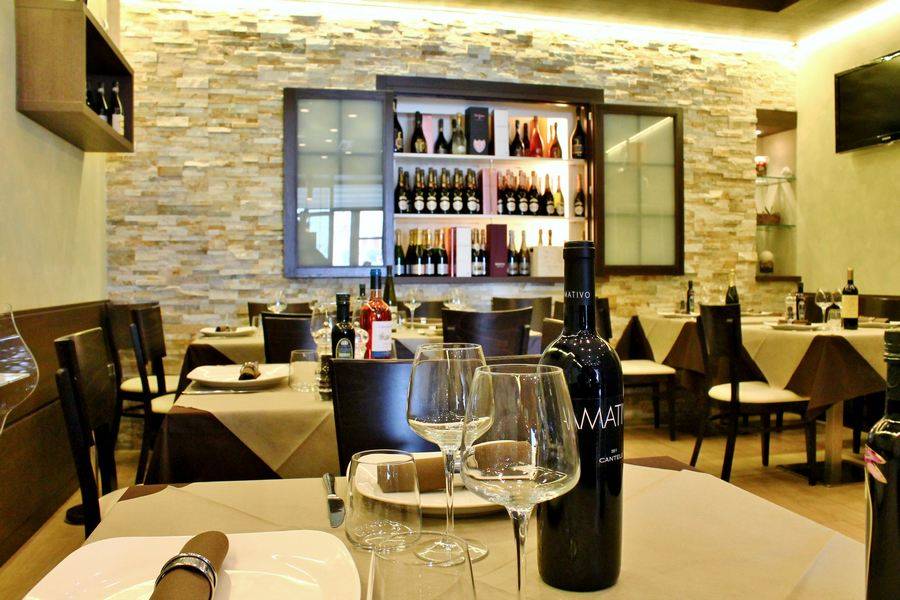 Interno di un ristorante con tavoli apparecchiati per cenare e una vetrina per i vini sulla parete.