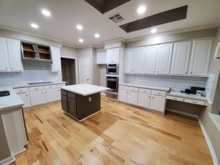 A kitchen with white cabinets and hardwood floors and a large island in the middle.