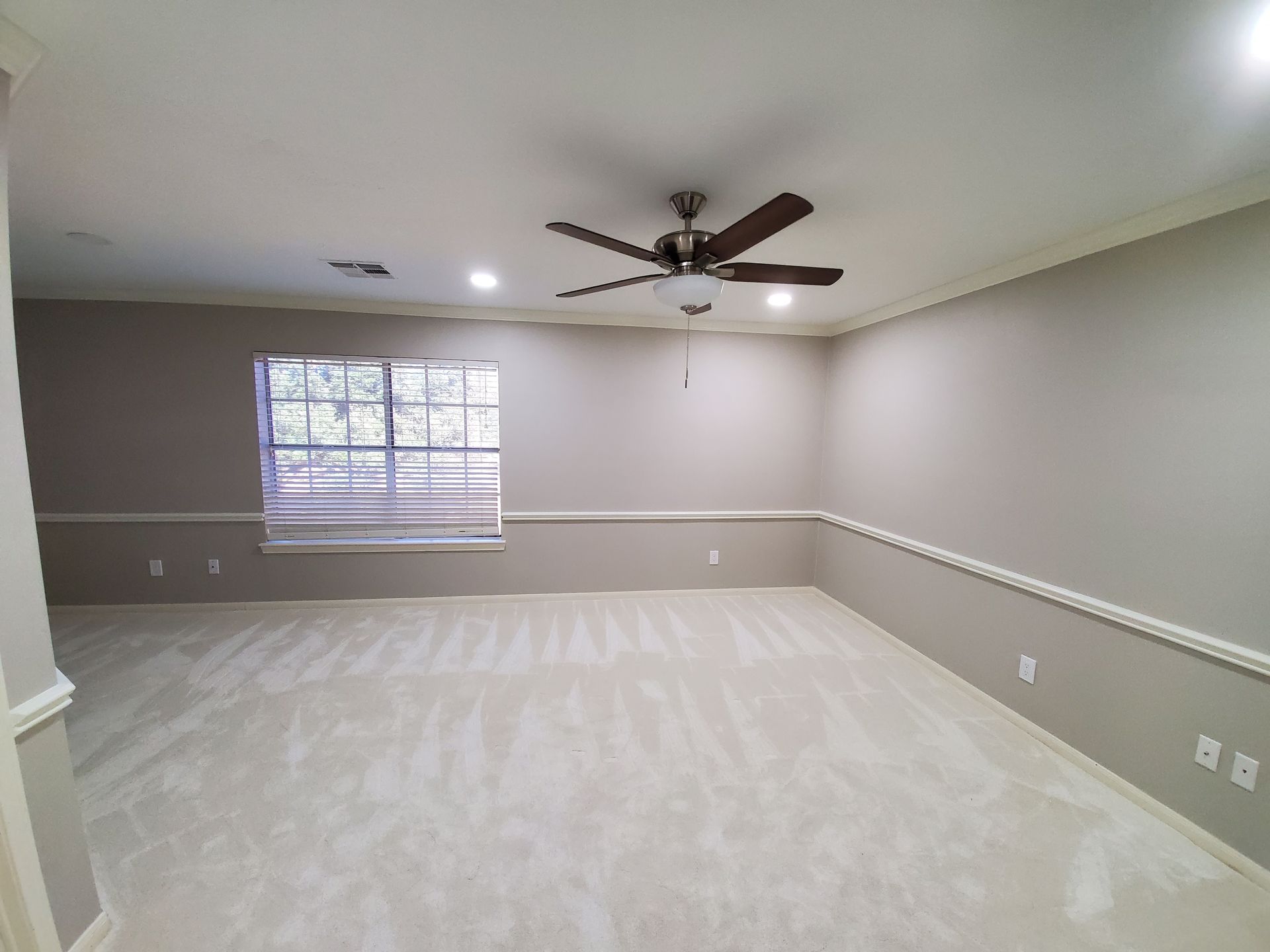 An empty living room with a ceiling fan and a window.