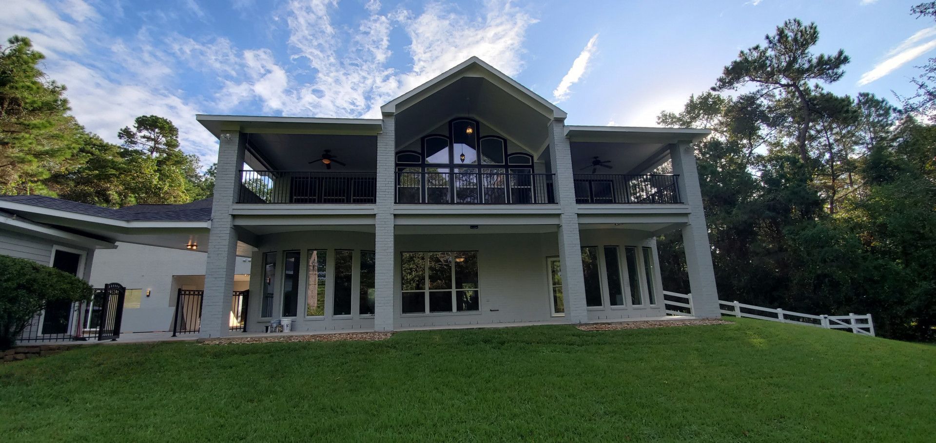 A large white house is sitting on top of a lush green hill surrounded by trees.