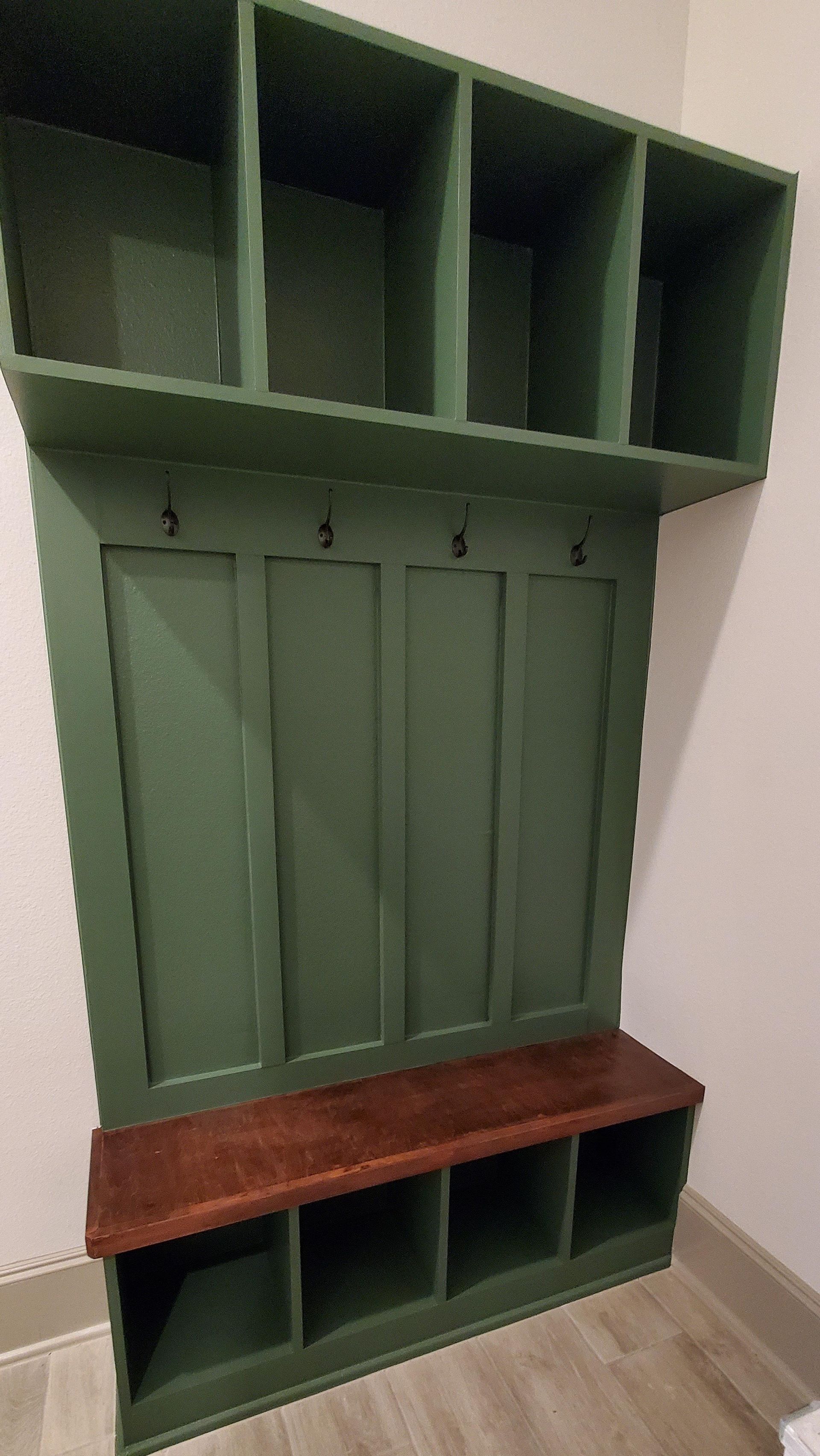 A green coat rack with a wooden bench in a room.