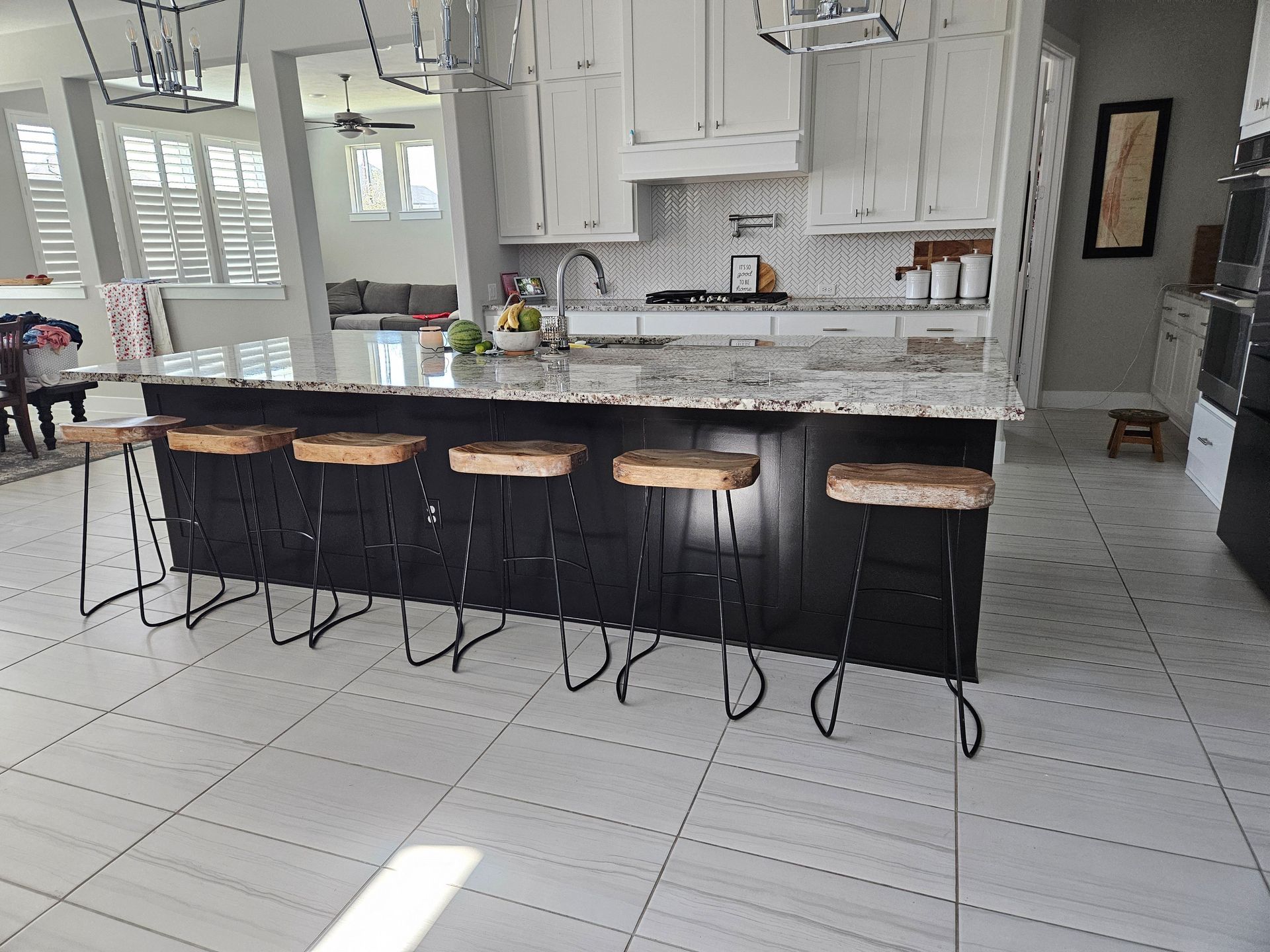 Modern kitchen with a black island, white cabinets, granite countertops, and rustic bar stools.