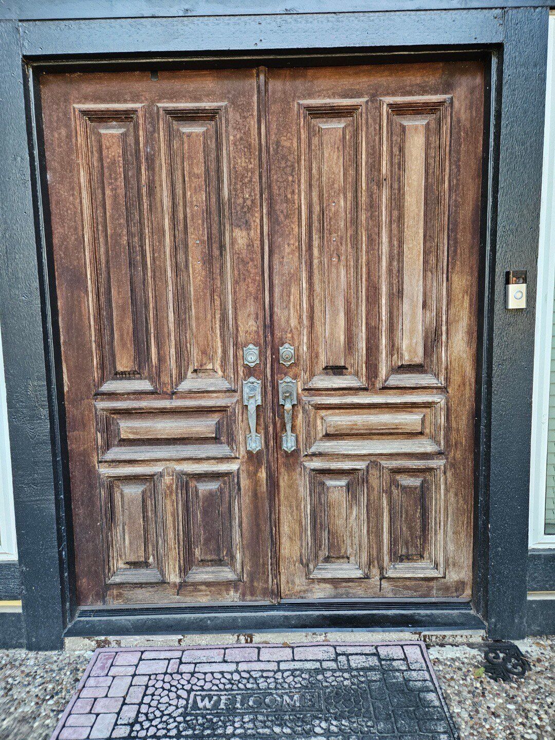 A large wooden door with a black frame is sitting on a brick walkway.