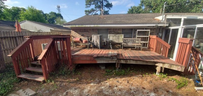 A wooden deck with stairs leading up to it is in the backyard of a house.