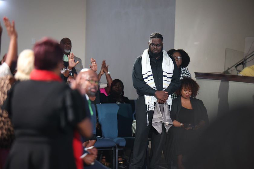 Audience applauding a man standing on stage with a white scarf in a dim indoor venue
