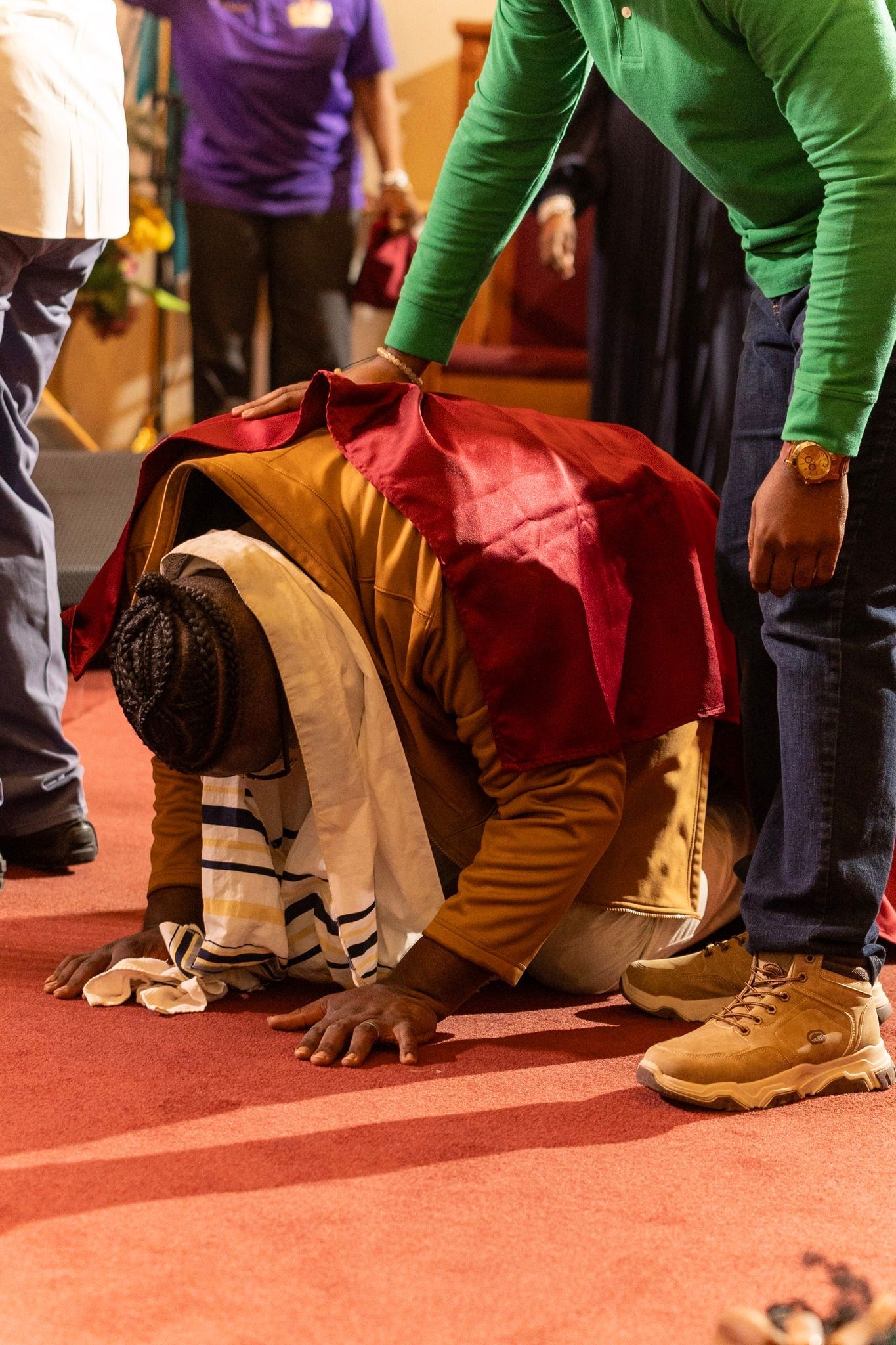 Person in a red and gold outfit kneels on a red carpet while others stand nearby.