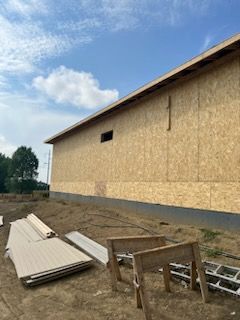 Construction site: exterior of building with exposed wood siding, blue sky. Lumber and saw horses in foreground.