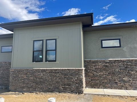 Modern building with stone base, green siding, black-framed windows against a blue sky.