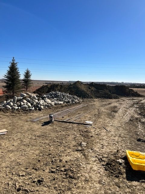 Dirt construction site with large piles of dirt and rocks under a blue sky.