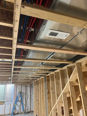Construction site interior. Exposed wooden beams, framing, and ventilation. Red and blue pipes visible.