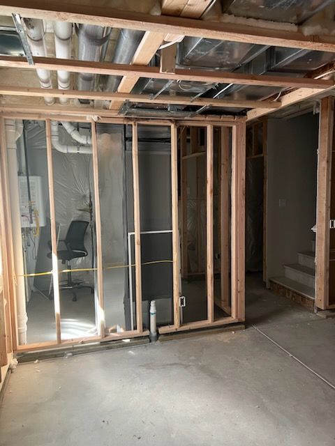 Framed walls in a basement under construction, concrete floor, exposed pipes and ceiling beams.
