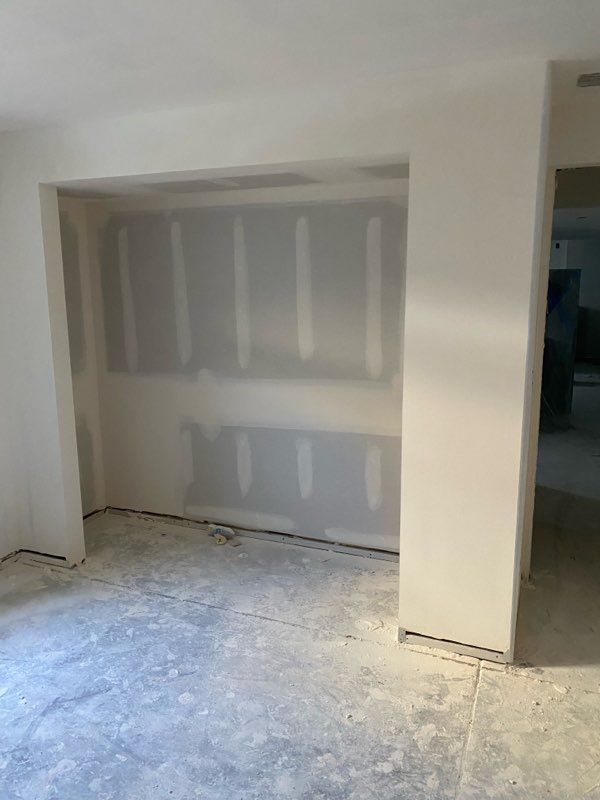 Room under construction with drywall installed.  Concrete floor and white walls. Open doorway on right.