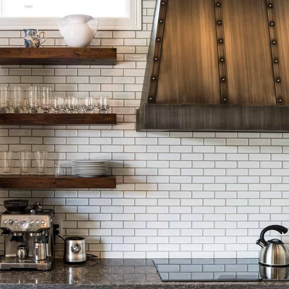 Kitchen with white brick backsplash, wooden shelves, and stainless appliances.