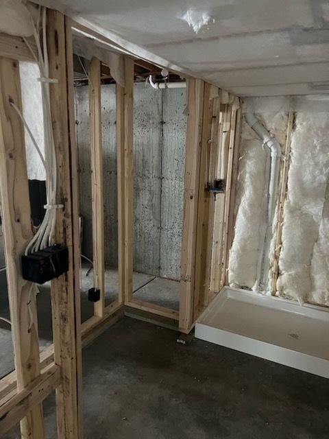 Basement framing with exposed studs, electrical wiring, and insulation. A concrete floor and shower base are visible.