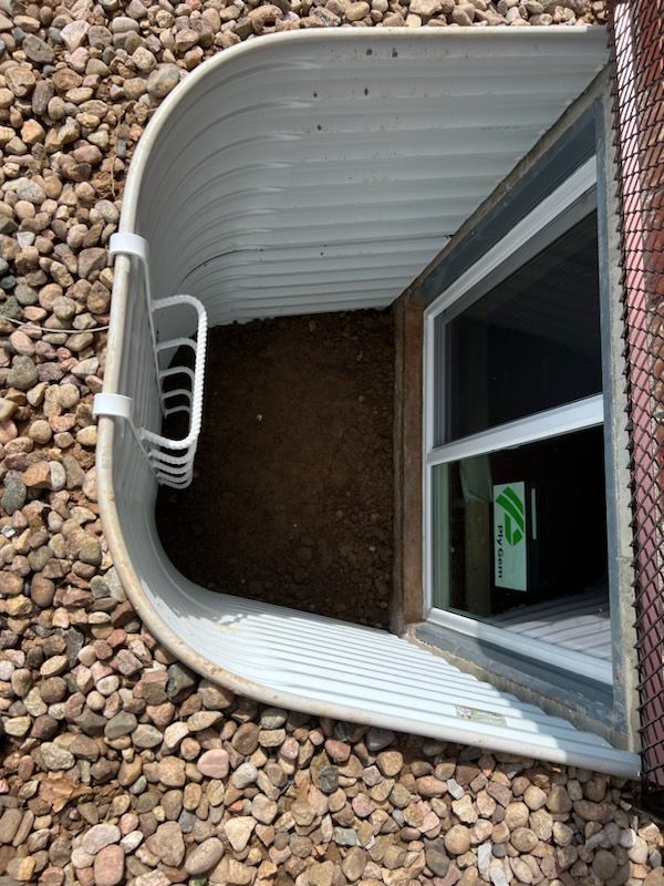 White window well with a window, gravel, and a hanging ladder.