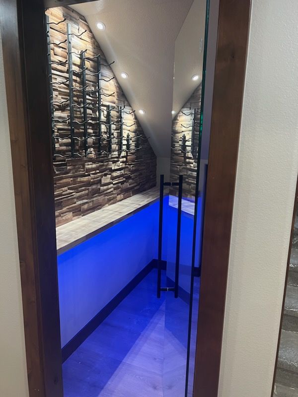 Glass-doored wine cellar with stone accent wall, blue lighting, and wood trim.