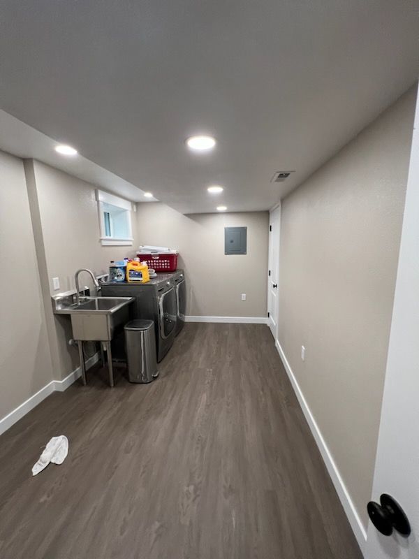 Laundry room with washer/dryer, stainless steel sink, tan walls, and wood-look flooring.