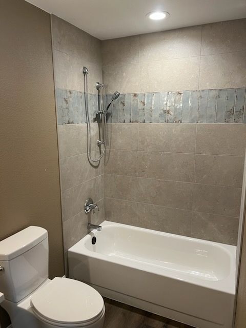 Bathroom with a white tub, tile shower surround, and toilet. Light beige walls.