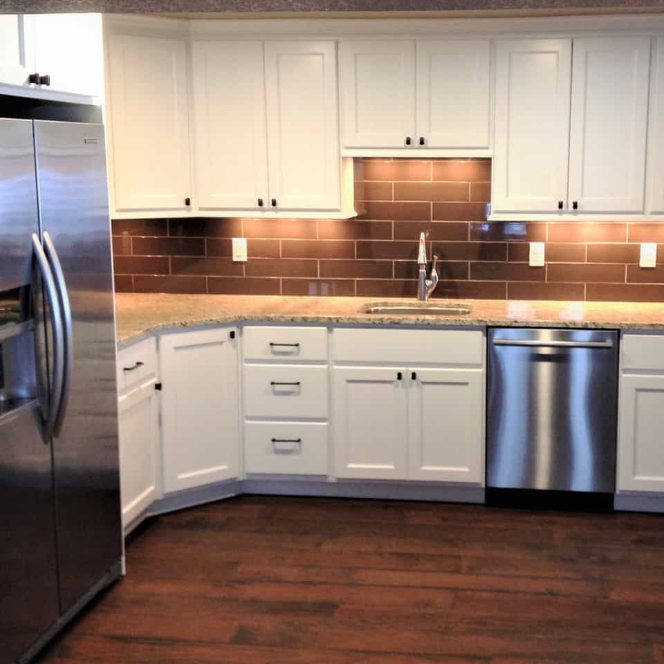 White kitchen cabinets, stainless steel appliances, and brown tile backsplash.