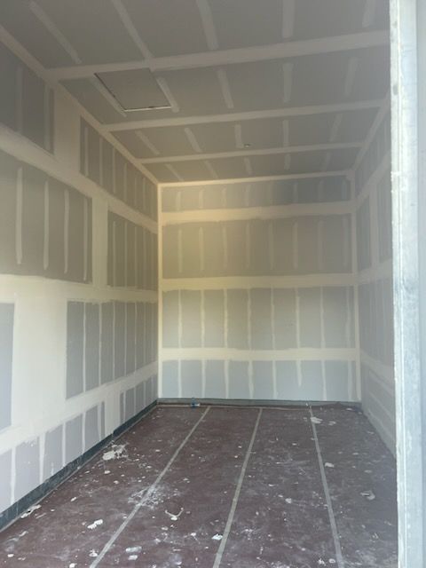 Interior of a room under construction with drywall on the walls and ceiling, brown floor, empty space.