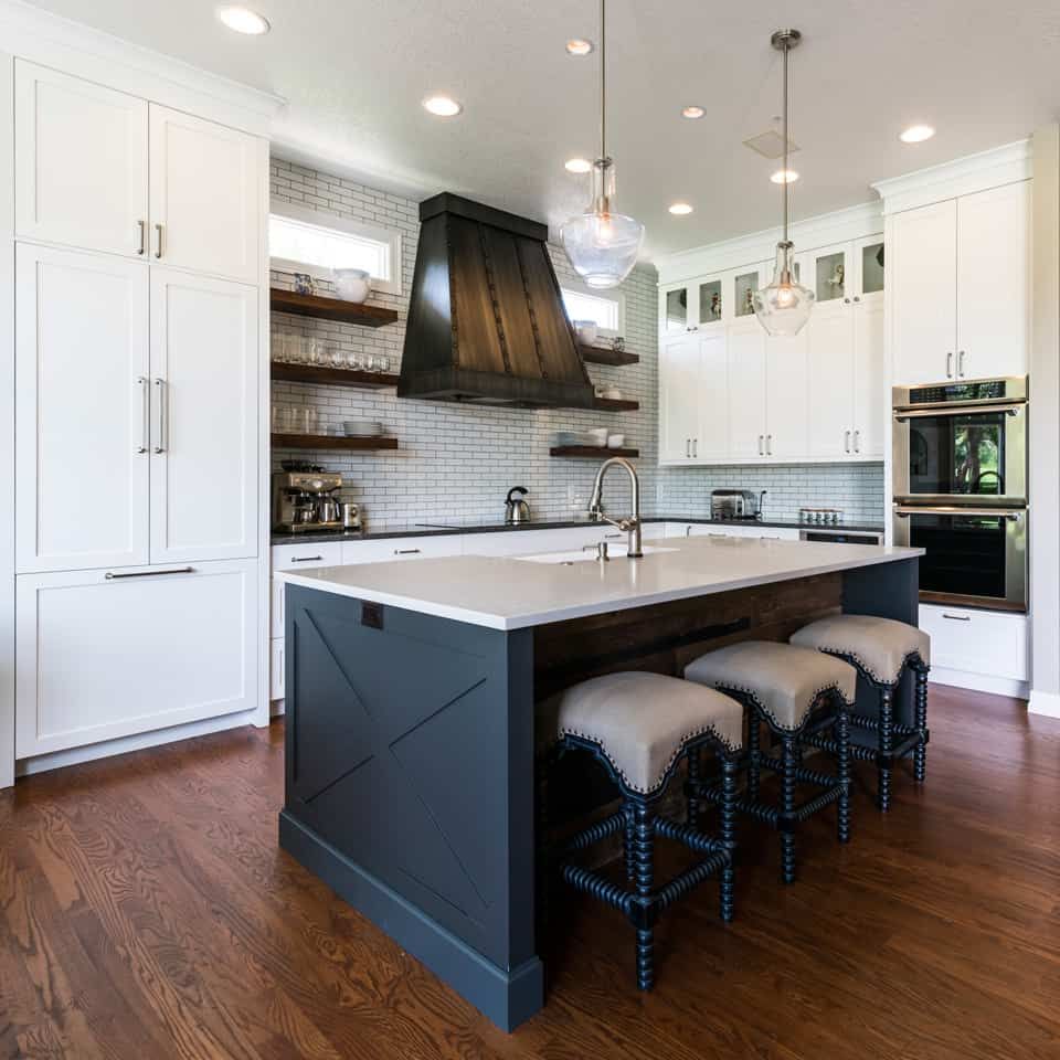 Stylish kitchen with white cabinets, dark blue island, and wooden floors.