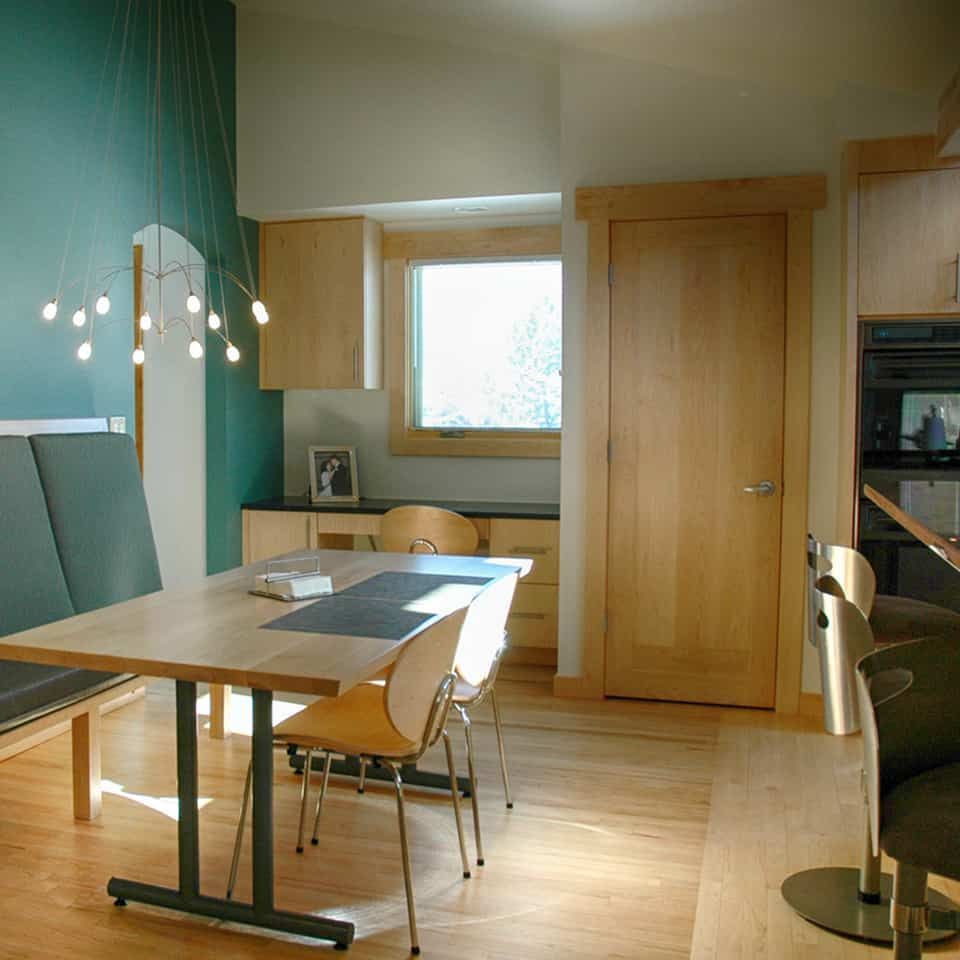 Dining area with teal wall, wooden table and chairs, and light fixture.