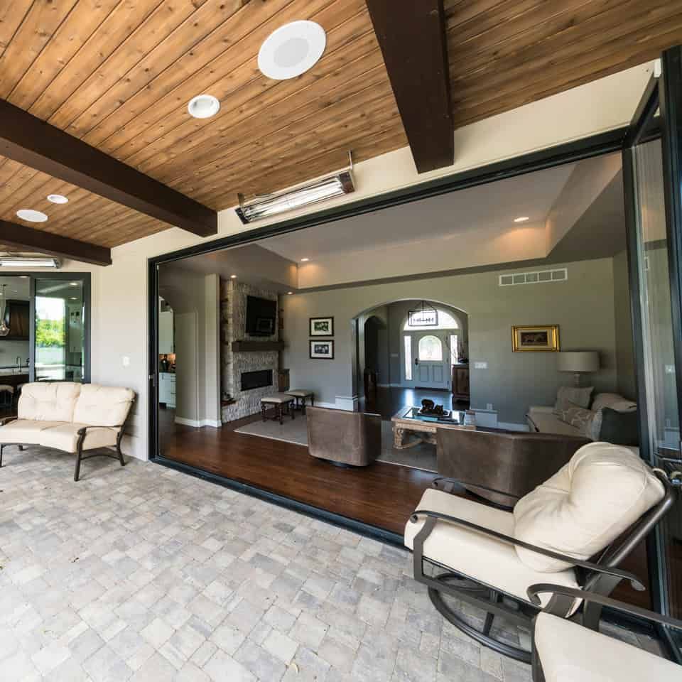 Patio with open door into living room. Light wood ceiling, stone patio, indoor seating.
