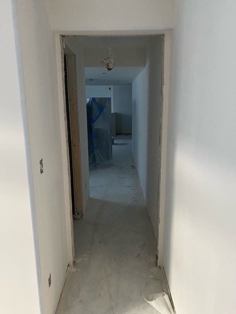 Interior doorway leading into a hallway, walls and floor unfinished, white paint, construction debris.