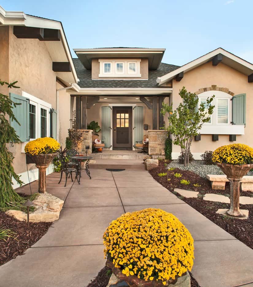 Beige stucco home with a walkway, adorned with yellow flowers, and a dark brown front door.
