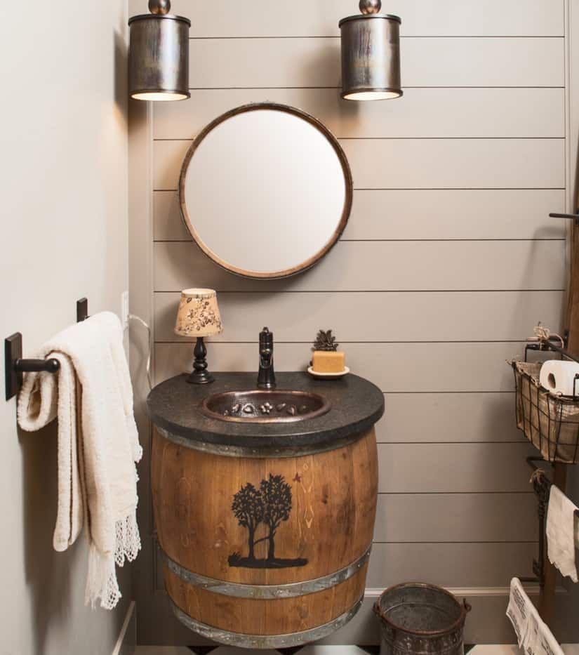 Rustic bathroom with a barrel sink, round mirror, sconce lighting, and a towel rack.