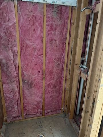 Framed shower stall with pink insulation, plumbing, and a drain in a bathroom.