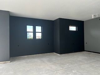 Empty room with concrete floor, dark gray walls, two windows, and white ceiling.
