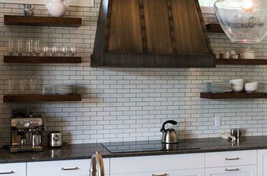 Kitchen with white subway tile, wooden shelves, stainless appliances, and a copper range hood.
