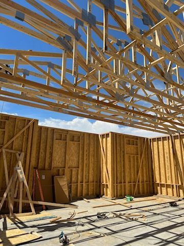 Construction site: wooden roof trusses and wall frames against a blue sky.