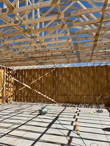 Wooden building frame with exposed trusses and walls, under a bright blue sky.