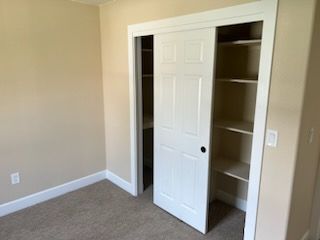 Closet with sliding white door, open to reveal shelves. Beige walls and carpet.