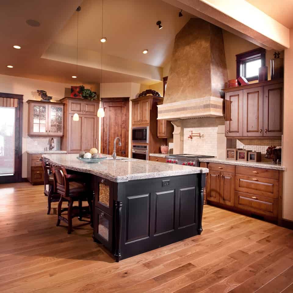 Rustic kitchen with wood cabinets, black island, granite countertop, and stone range hood.