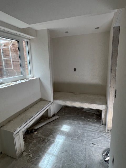 Unfinished room with built-in benches and window. White walls and cement floor.